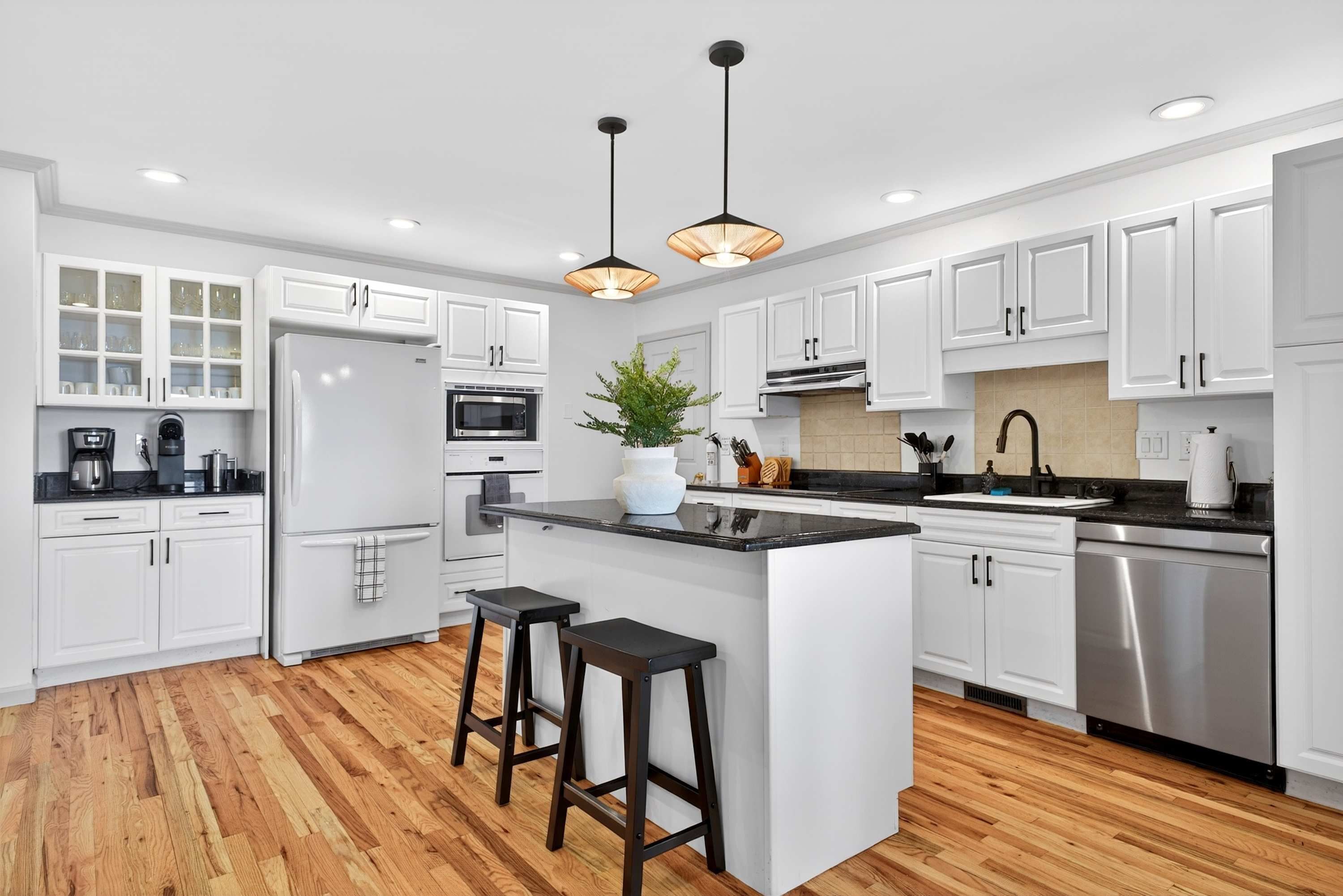 A modern kitchen with white cabinets, a central island, stainless steel appliances, and wooden flooring.