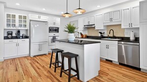 A modern kitchen with white cabinets, a central island, stainless steel appliances, and wooden flooring. - Luxury Mtn Retreat Hot Tub Sleeps 18 Game Room (Asheville)