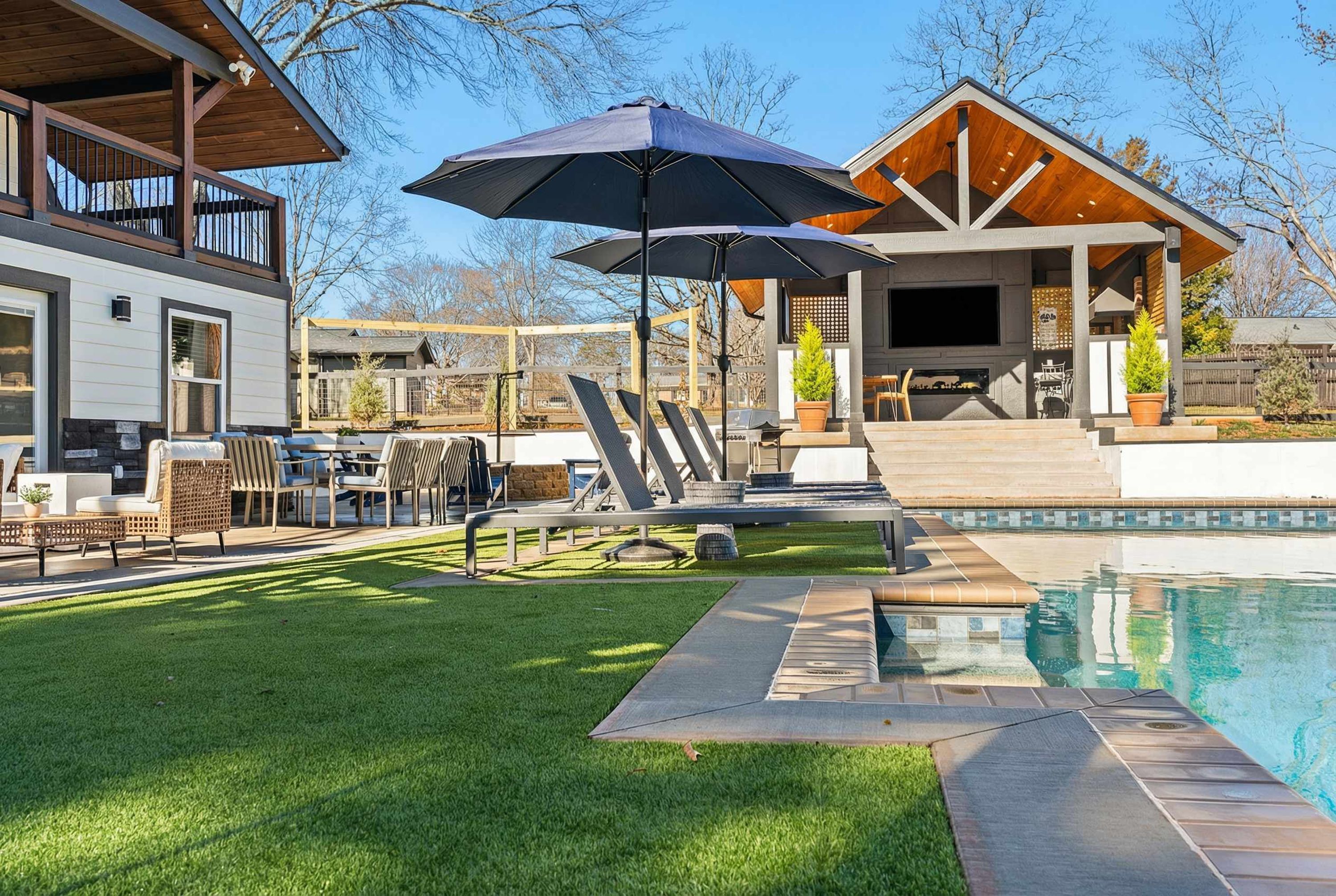 A modern outdoor pool area with a lounge chair, umbrella, and a dining setup.