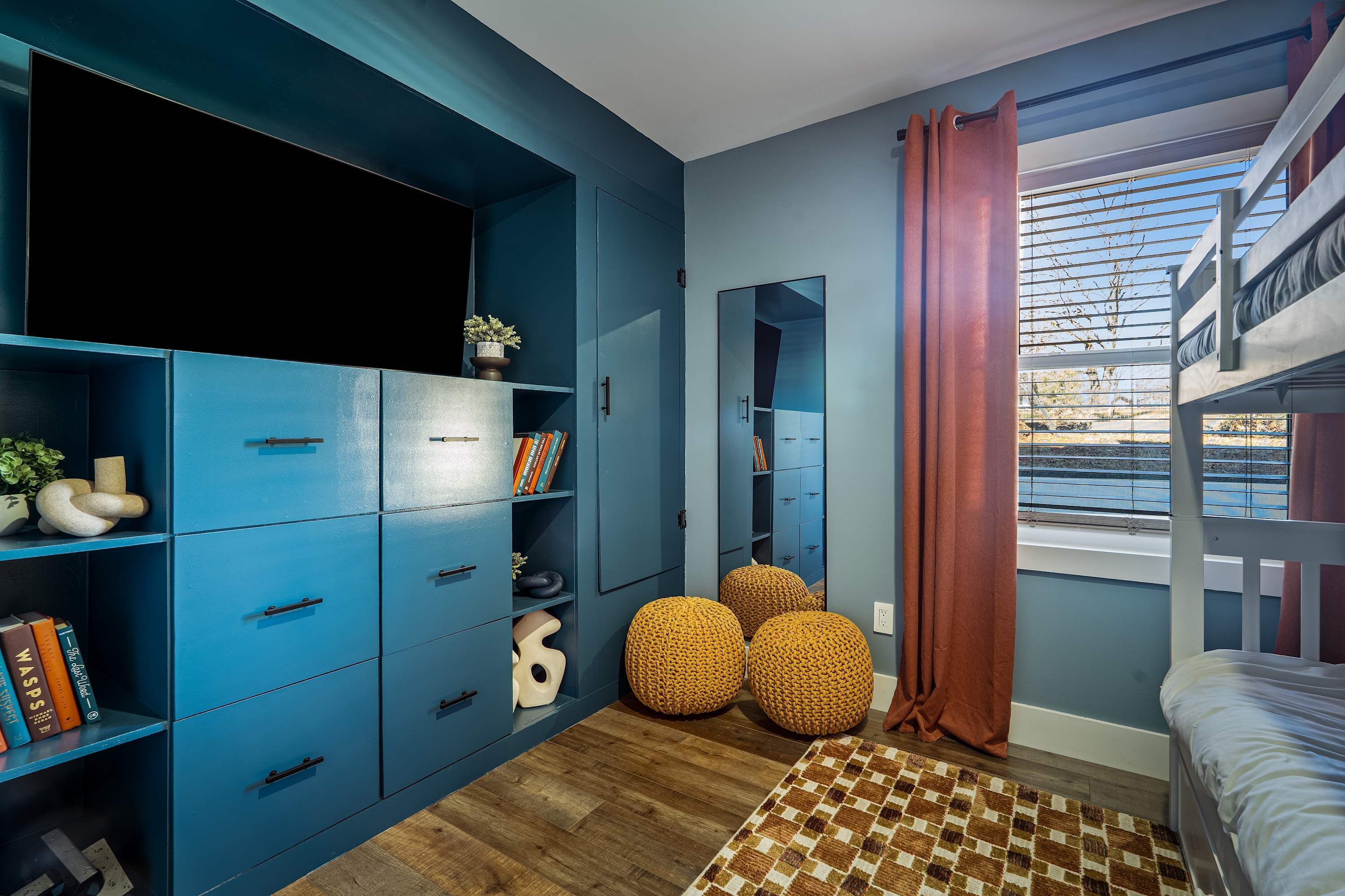 Un dormitorio con una cama individual doble, un armario azul, un espejo y vistas al exterior.