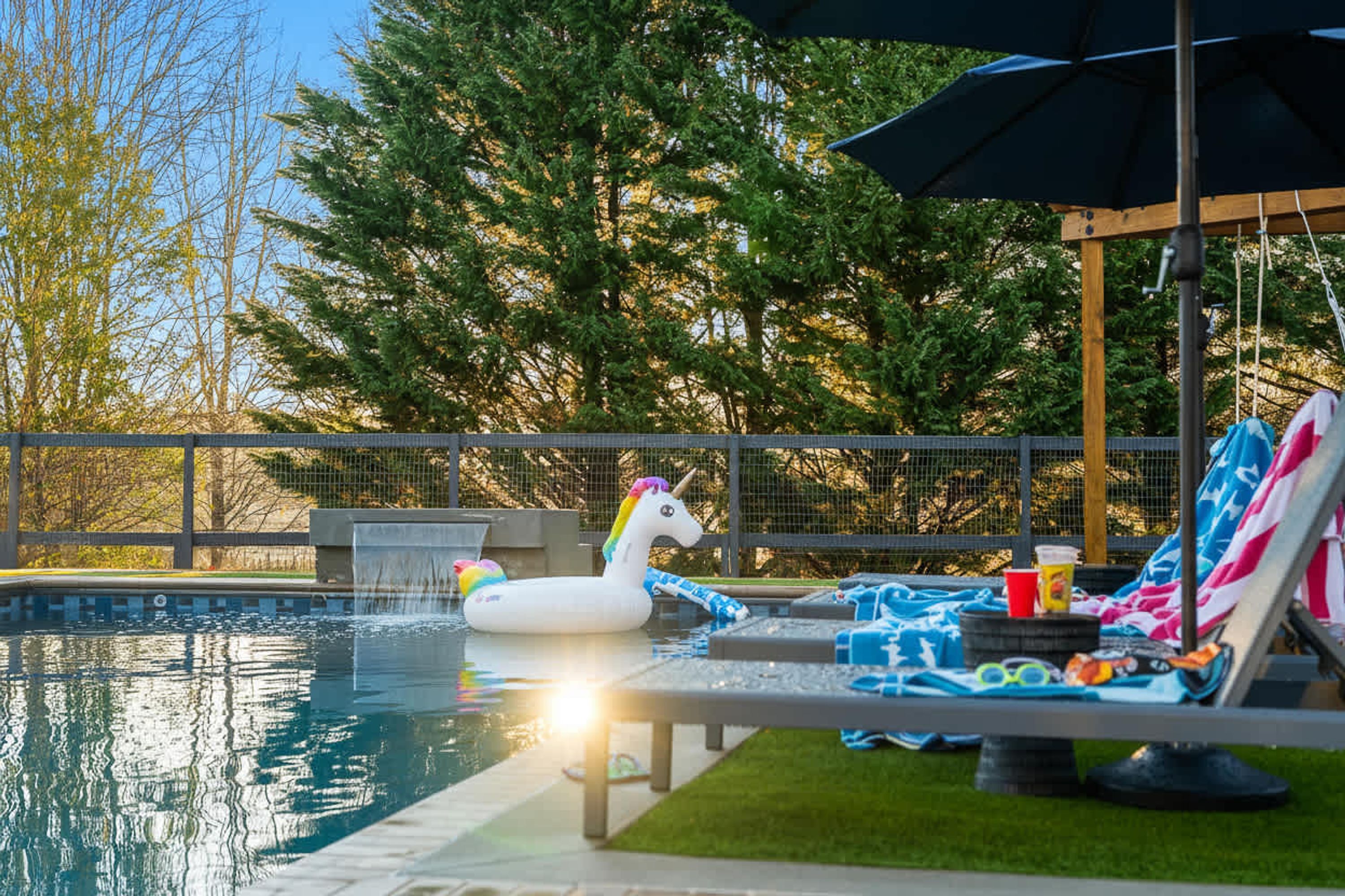 A swimming pool with a unicorn float, lounge chairs, and an umbrella.