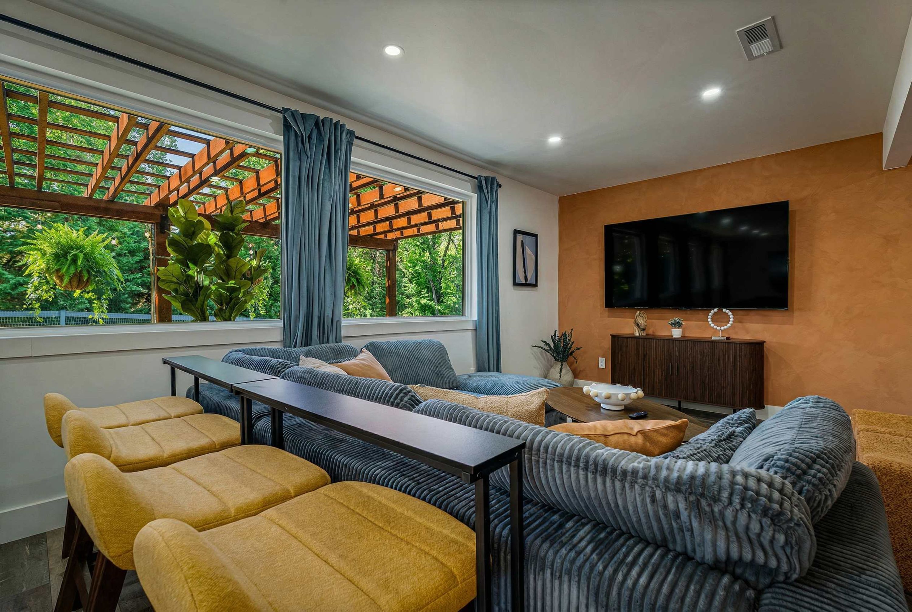 A modern living room with a sofa set, a dining table, and a TV mounted on the wall.