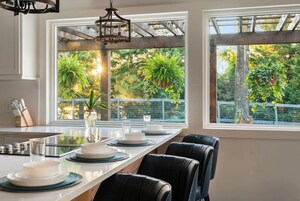 Una cocina moderna con una isla grande, encimeras blancas y vistas a un jardín exuberante a través de amplios ventanales.
