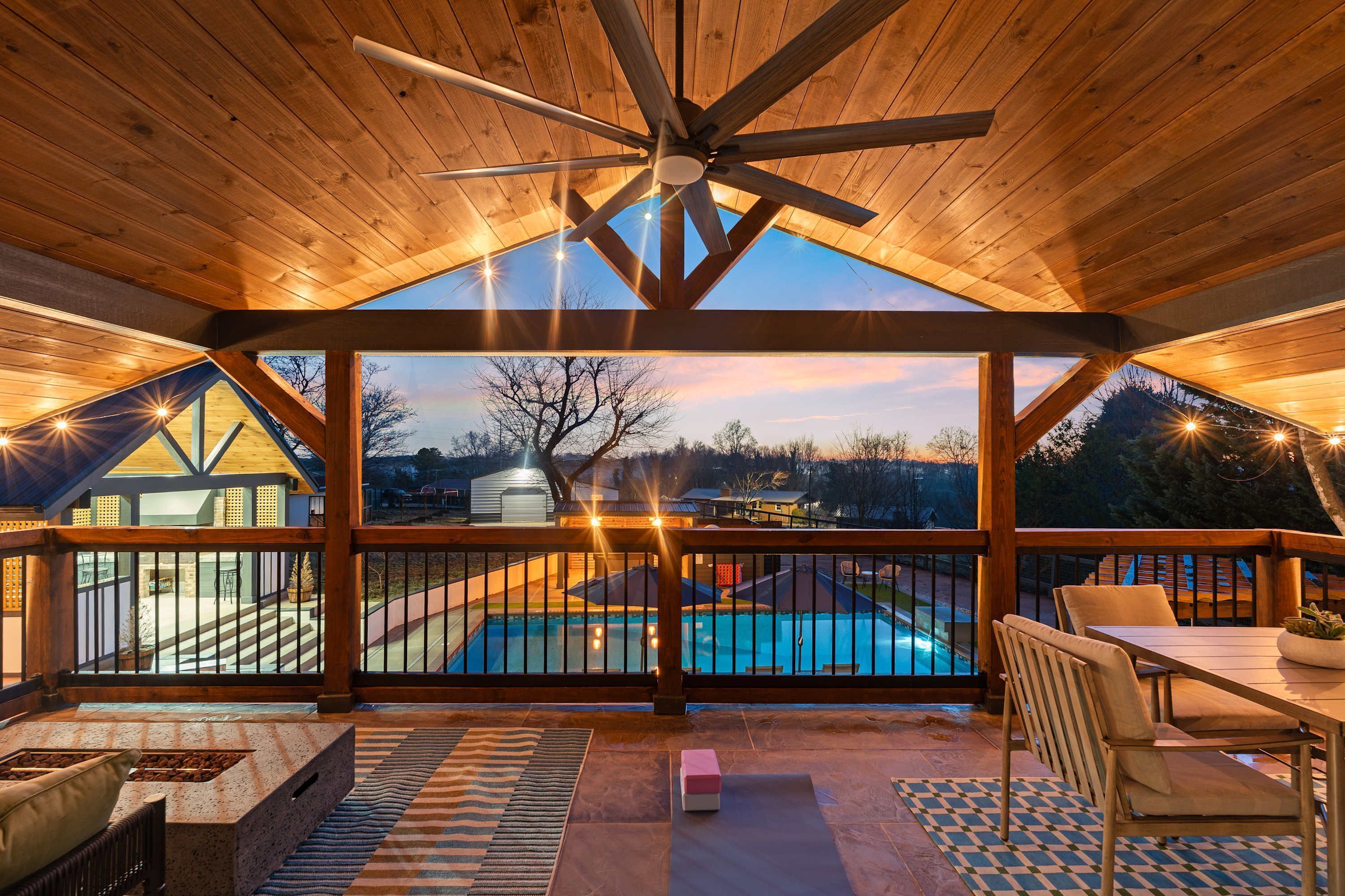 A covered outdoor area with a pool, wooden deck, and a view of the surrounding landscape.