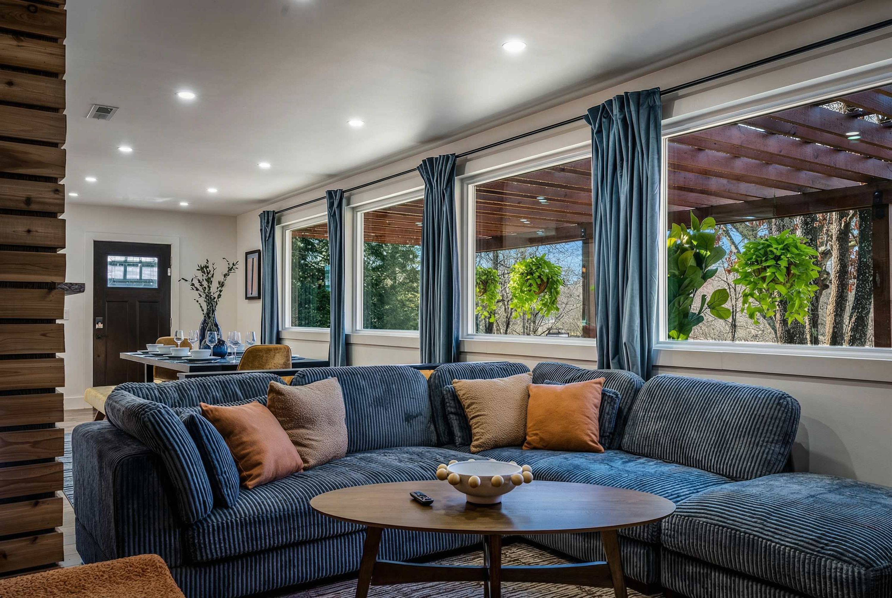 A modern living room with a sectional sofa, a round coffee table, and large windows with curtains.