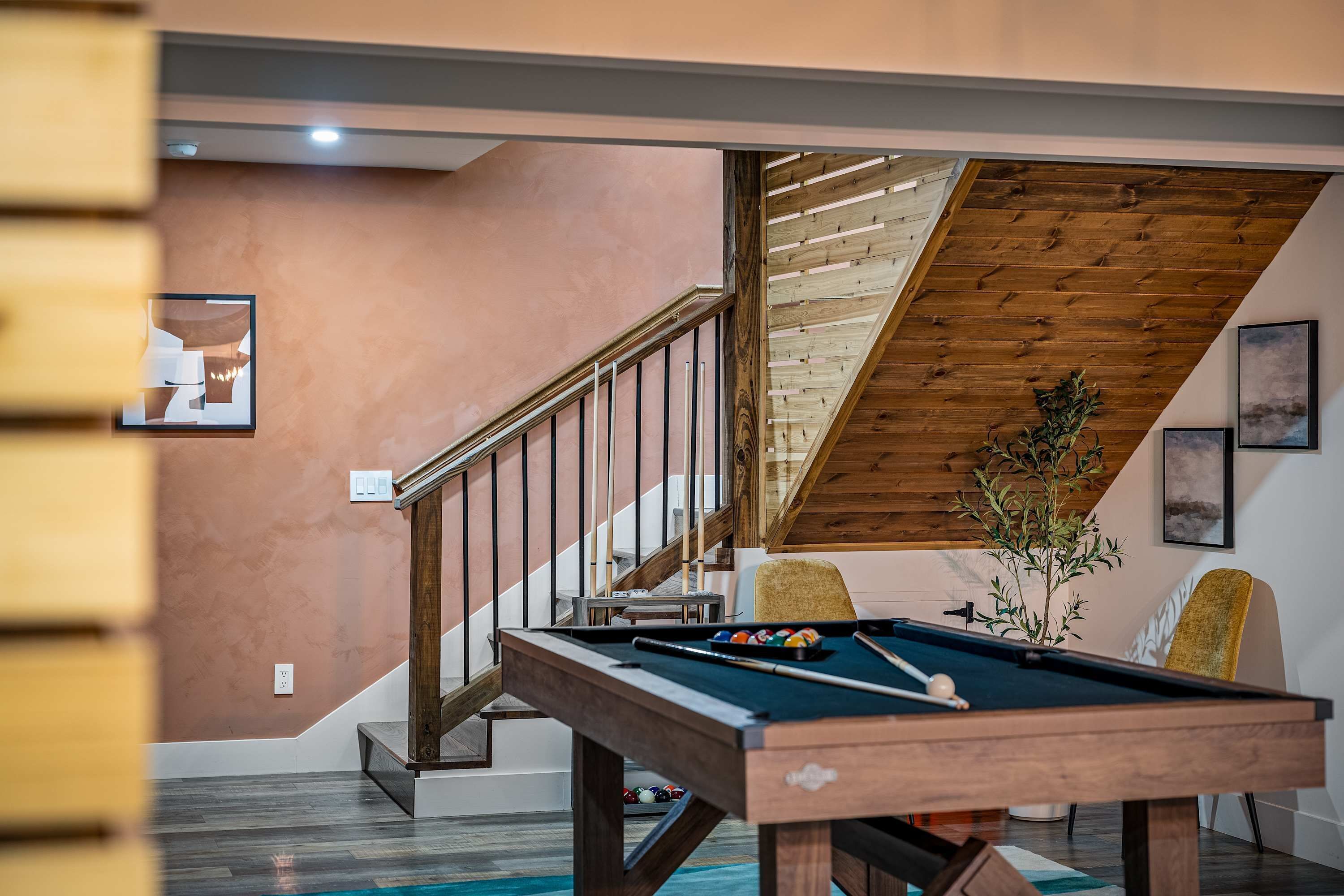 A pool table in a room with a wooden staircase and a view of the outdoors.