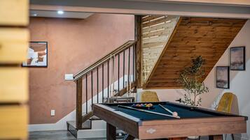 A pool table in a room with a wooden staircase and a view of the outdoors.