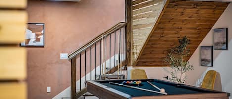 A pool table in a room with a wooden staircase and a view of the outdoors.
