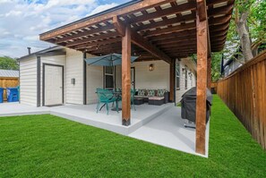 A covered patio area with a table and chairs, a grill, and a wooden fence. - Family Friendly Patio Fireplace BBQ Games (San Antonio)