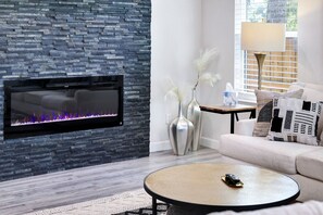 Una sala de estar moderna con una pared de piedra, una chimenea, un sofá, una mesa de centro y jarrones decorativos.