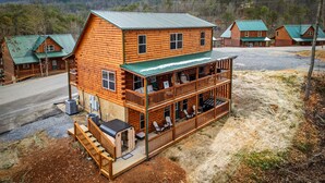 A log cabin with a two-story porch, outdoor seating, and a view of the surrounding forest. - Smoky Mtn Retreat Sauna Hot Tub Game Room (Pigeon Forge)