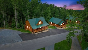 A lodge with multiple cabins, each featuring a green roof and wooden exterior, surrounded by dense forest. - Smoky Mtn Retreat Sauna Hot Tub Game Room (Pigeon Forge)
