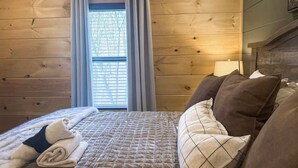 A wooden-paneled room with a bed, a window with curtains, and a headboard. - Smoky Mtn Retreat Sauna Hot Tub Game Room (Pigeon Forge)