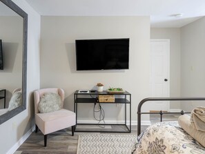 Quarto moderno com cama, cadeira, televisão e mesa de cabeceira.