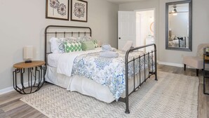 A bedroom with a bed, a bedside table, a lamp, a ceiling fan, a mirror, and a door leading to another room. - Mountain Views Hot Tub Firepit Game Room (Asheville)