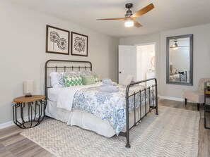 A bedroom with a bed, a bedside table, a lamp, a ceiling fan, a mirror, and a door leading to another room. - Mountain Views Hot Tub Firepit Game Room (Asheville)