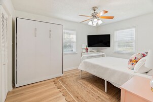 Un dormitorio con cama, televisor, armario y ventilador de techo.