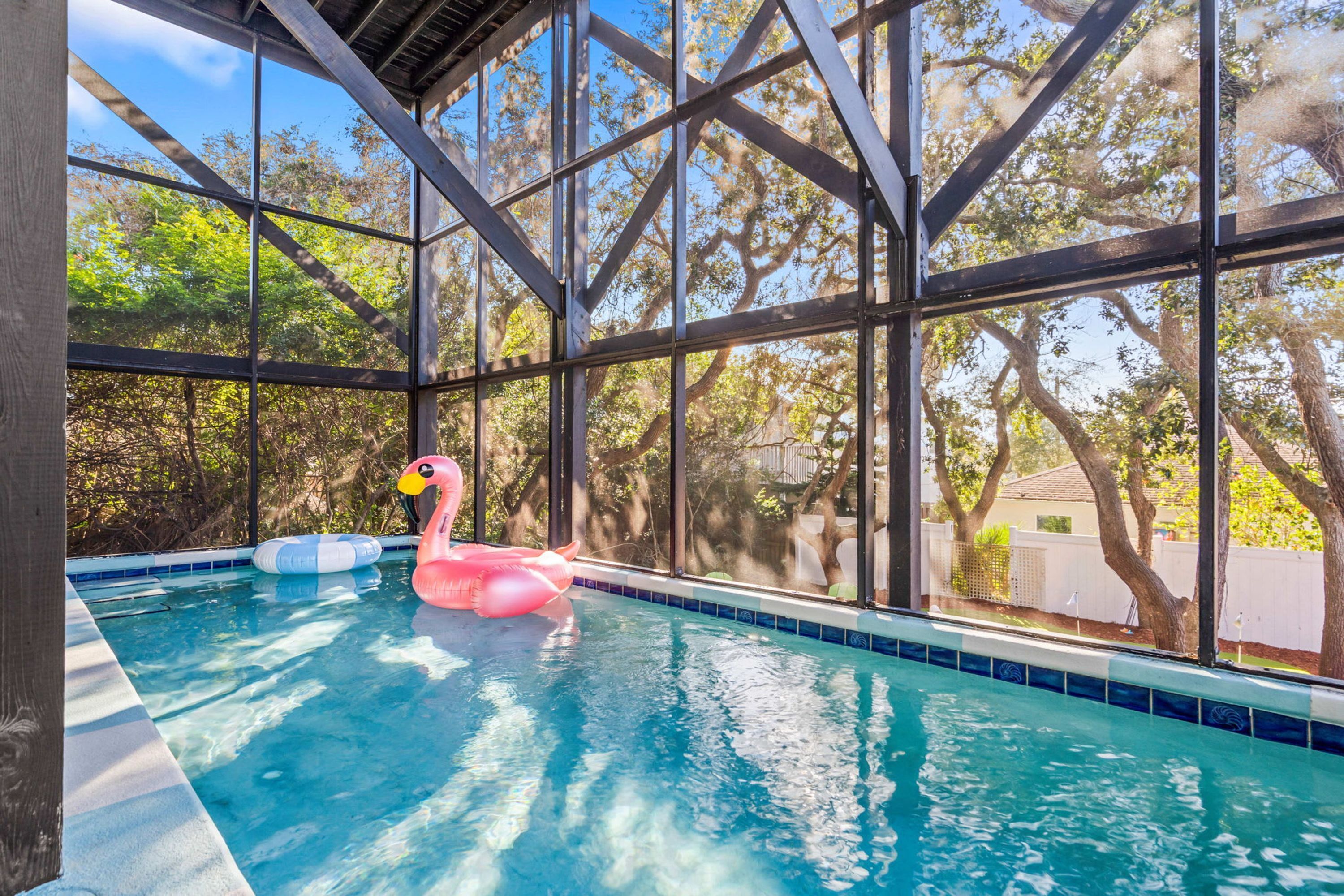 An indoor swimming pool with clear glass walls, a pink flamingo float, and a blue and white inflatable ring.