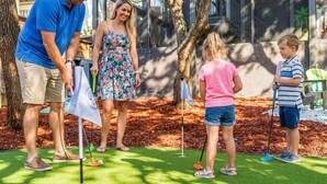 Eine Familie spielt Golf auf einem gepflegten Rasen, im Hintergrund ein modernes Gebäude.