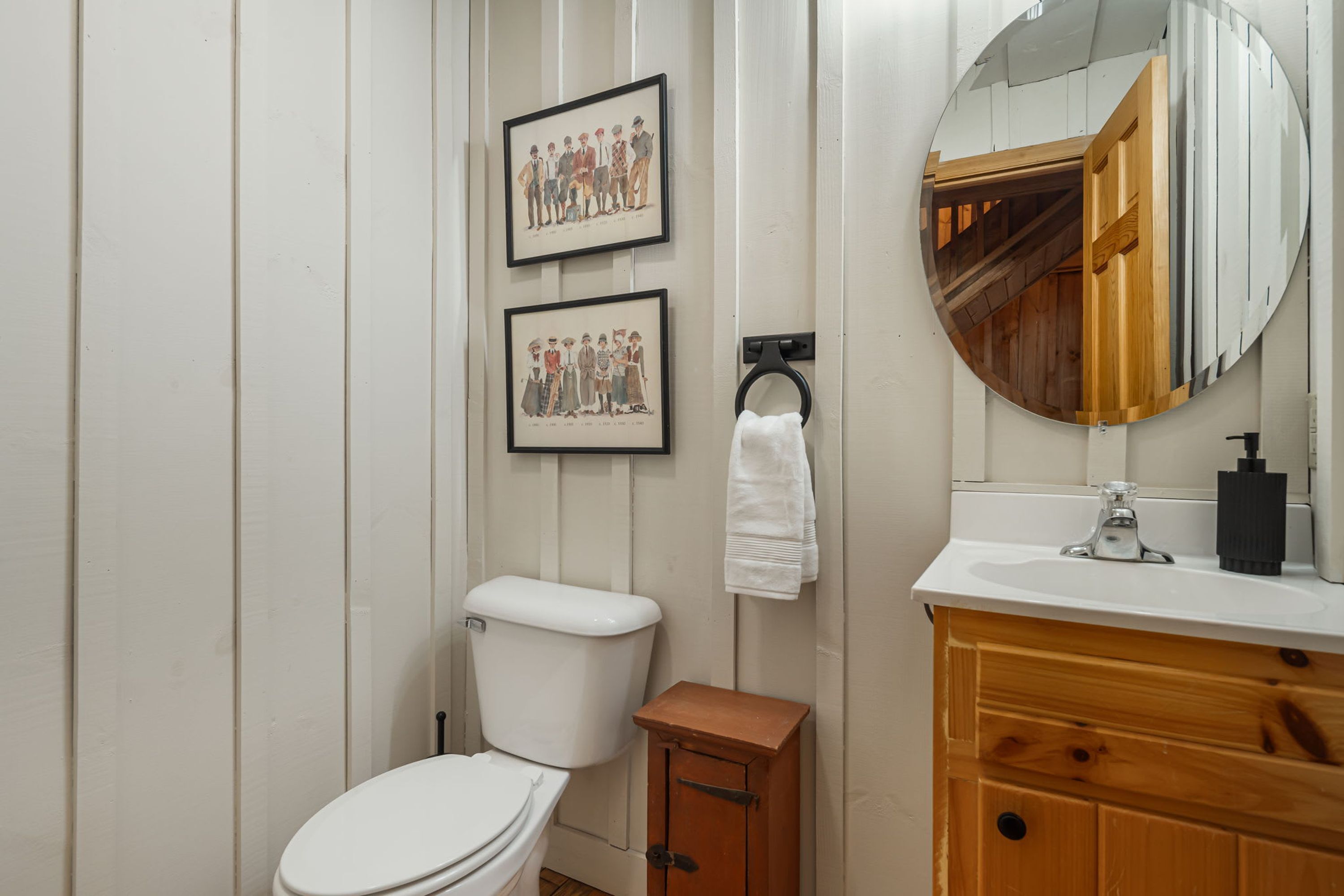 Un bagno con il water, un armadietto in legno, un lavandino, uno specchio e due quadri appesi al muro.