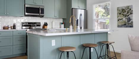 A modern kitchen with teal cabinets, stainless steel appliances, and a large island with stools.