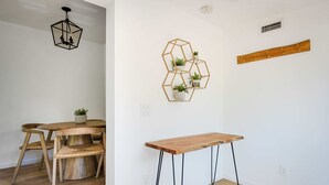 Een kamer met een houten eettafel, stoelen, een zeshoekige wanddecoratie met planten, een houten bank en een plafondlamp.