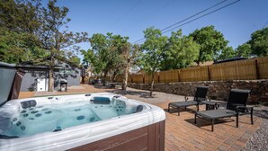Een achtertuin met een jacuzzi, terrasmeubilair en een stenen muur.