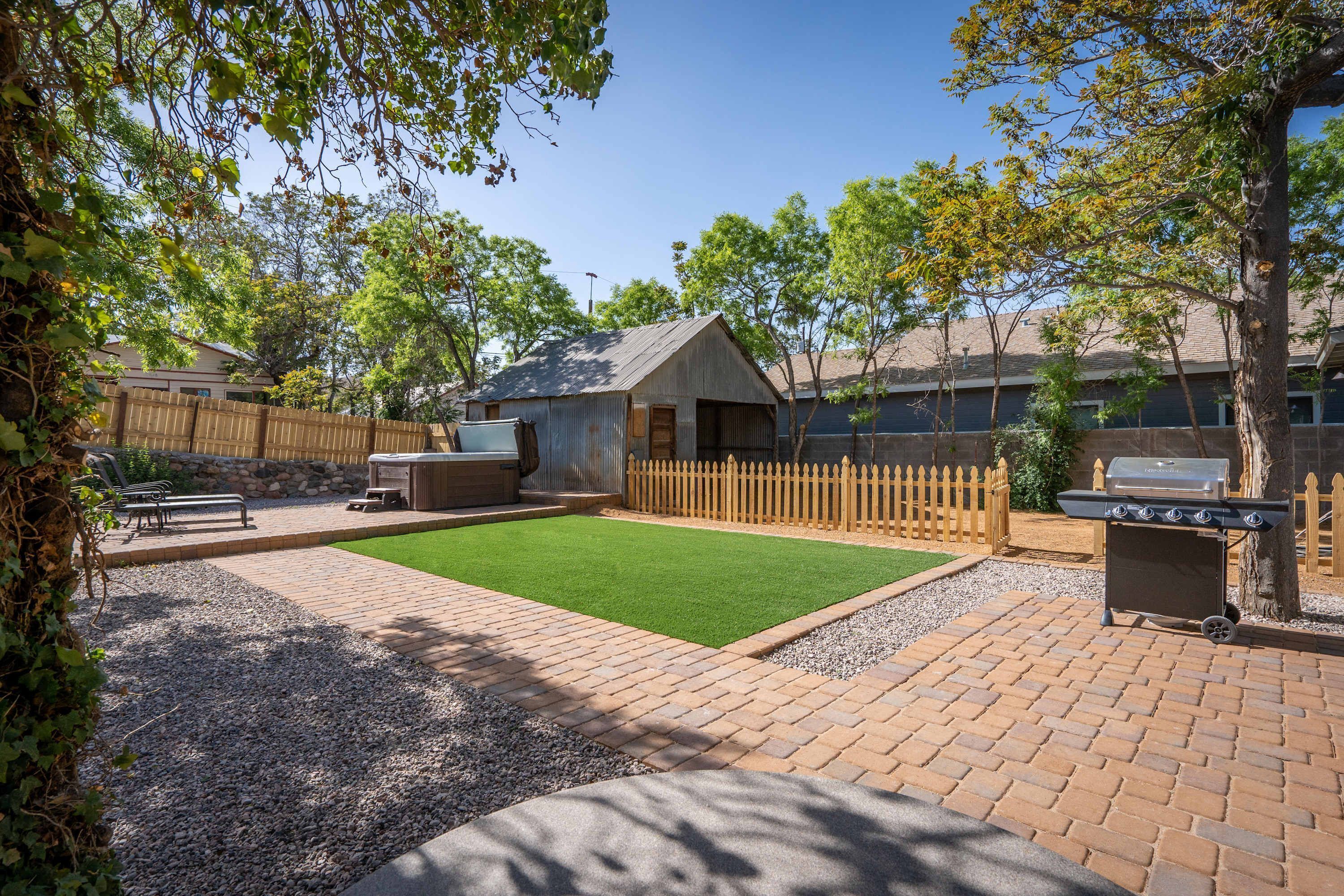 A backyard with a hot tub, barbecue grill, and a fenced play area.