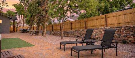 Une terrasse avec un sol en briques, deux fauteuils noirs, une petite table et un barbecue.