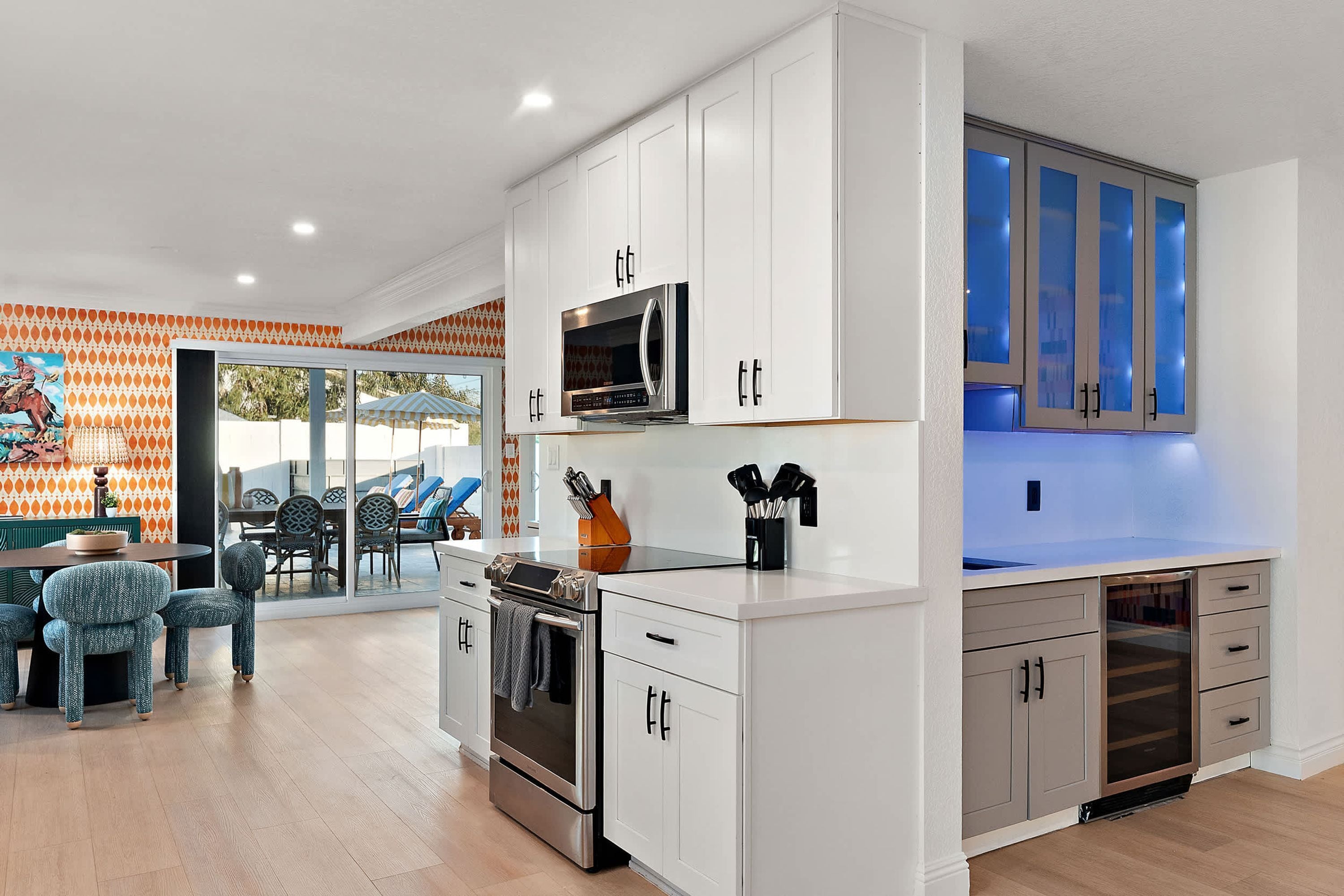 A modern kitchen with white cabinets, stainless steel appliances, and a dining area with a patterned wall and outdoor seating.