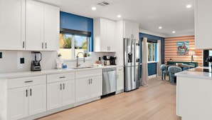 Una cucina moderna con mobili bianchi, elettrodomestici in acciaio inossidabile e una parete d'accento blu.