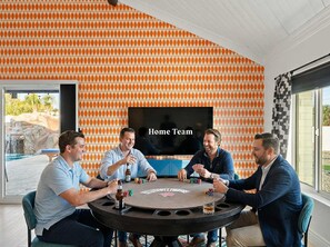 A group of people playing poker at a table with a 'Home Team' TV screen in the background. - The Desert Daydream Heated Pool Water Slide (Scottsdale)