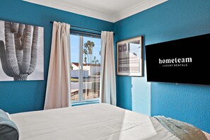A bedroom with a large bed, a window with curtains, and a wall-mounted TV displaying 'hometeam LUXURY RENTALS'. - The Desert Daydream Heated Pool Water Slide (Scottsdale)