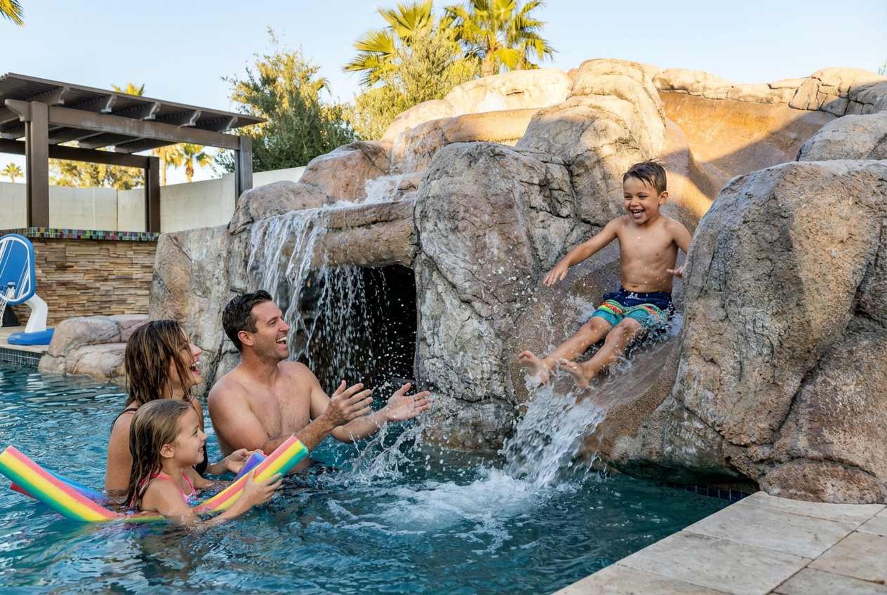 Ein Pool mit Felswasserfall, einer überdachten Sitzgelegenheit und blauem Himmel.