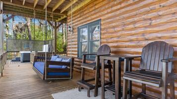 Une cabane en bois avec une terrasse, une balançoire, un canapé et une table avec des chaises.