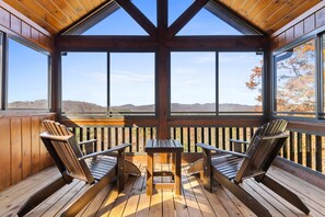 Una terraza de madera con una mesa y sillas, con vistas a un paisaje montañoso.