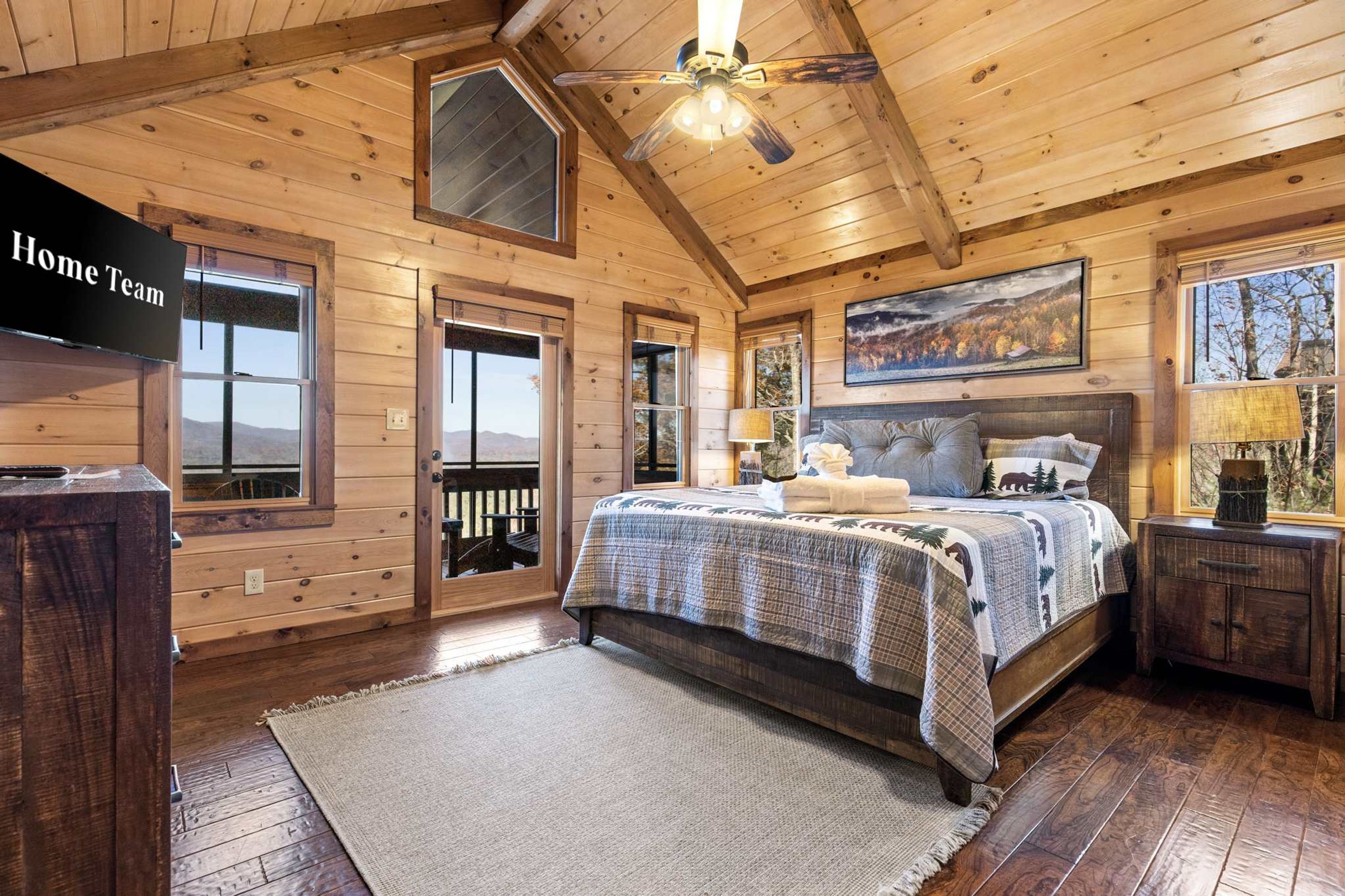 Une chambre située dans un chalet en rondins, avec un grand lit, un ventilateur de plafond et une vue sur les montagnes par les fenêtres.