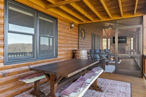 A wooden deck with a table and benches, large windows, and a view of the outside. - Family-friendly Cabin Hot Tub Games Views (Morganton)