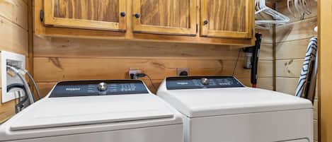Un lavadero con dos lavadoras Whirlpool blancas, armarios de madera arriba y un perchero con ganchos.