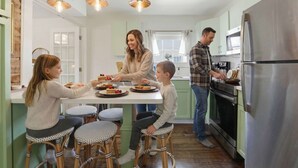A family dining in a modern kitchen with a central island, stainless steel appliances, and a view of the outdoors. - Charming Savannah Getaway Hot Tub Sleeps 8 (Savannah)