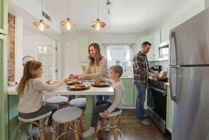 A family dining in a modern kitchen with a central island, stainless steel appliances, and a view of the outdoors. - Charming Savannah Getaway Hot Tub Sleeps 8 (Savannah)