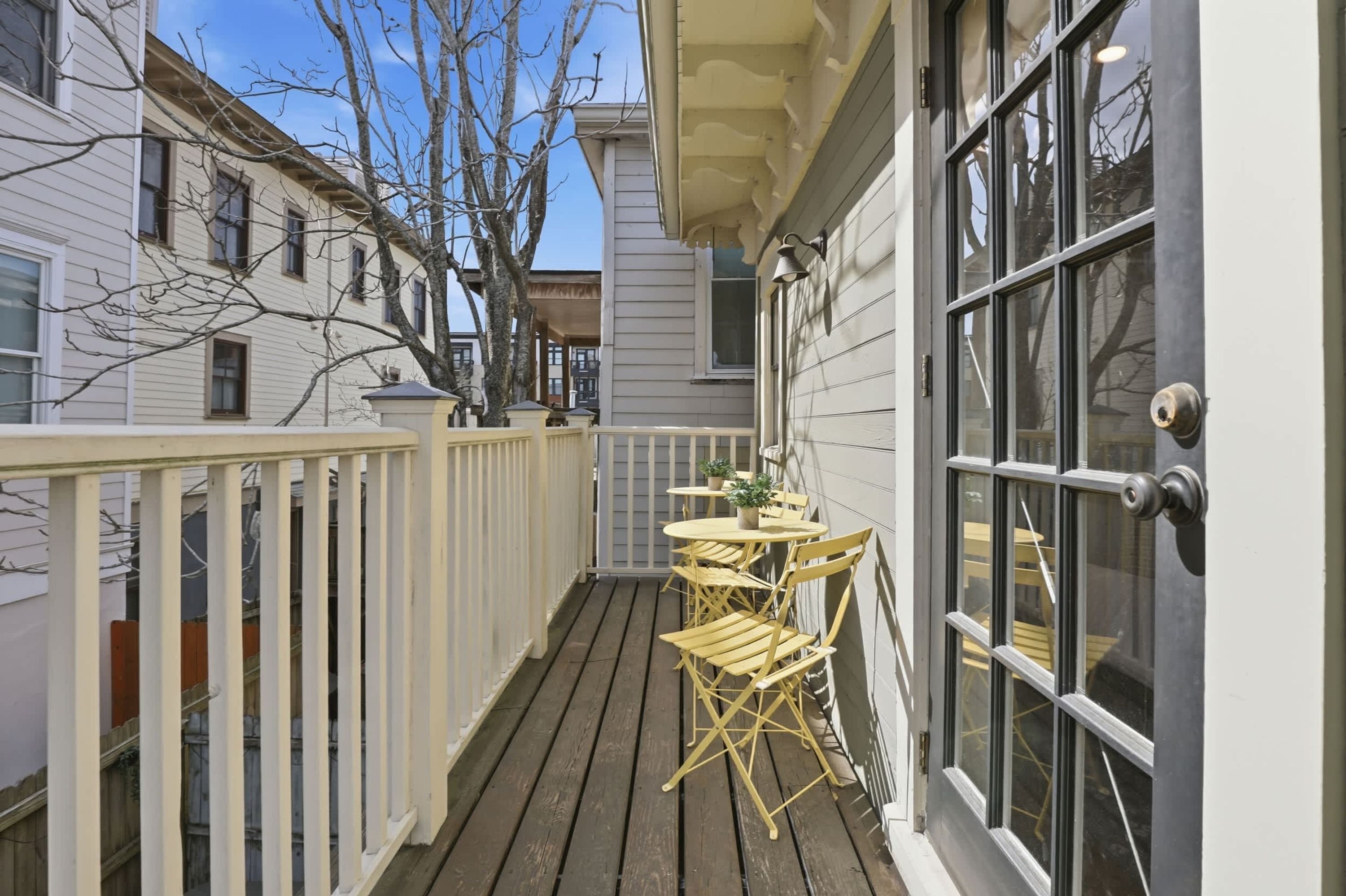 A wooden deck with a table and chairs, a white railing, and a door with a window.