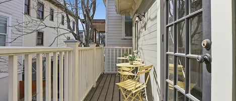 A wooden deck with a table and chairs, a white railing, and a door with a window.