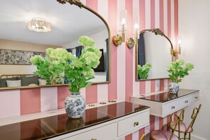 Une salle de bain avec un mur à rayures, une commode avec un miroir et un vase rempli de fleurs vertes.