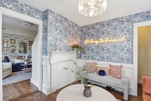 A room with floral wallpaper, a neon sign, a fireplace, and a seating area with cushions. - Charming Savannah Getaway Hot Tub Sleeps 8 (Savannah)