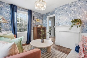 Une pièce avec une table ronde, un canapé, une cheminée et une fenêtre avec des rideaux.