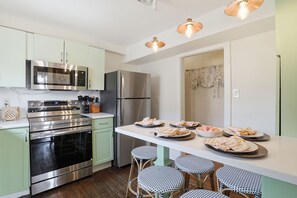 A modern kitchen with stainless steel appliances, a dining area with a white countertop, and wicker chairs. - Charming Savannah Getaway Hot Tub Sleeps 8 (Savannah)