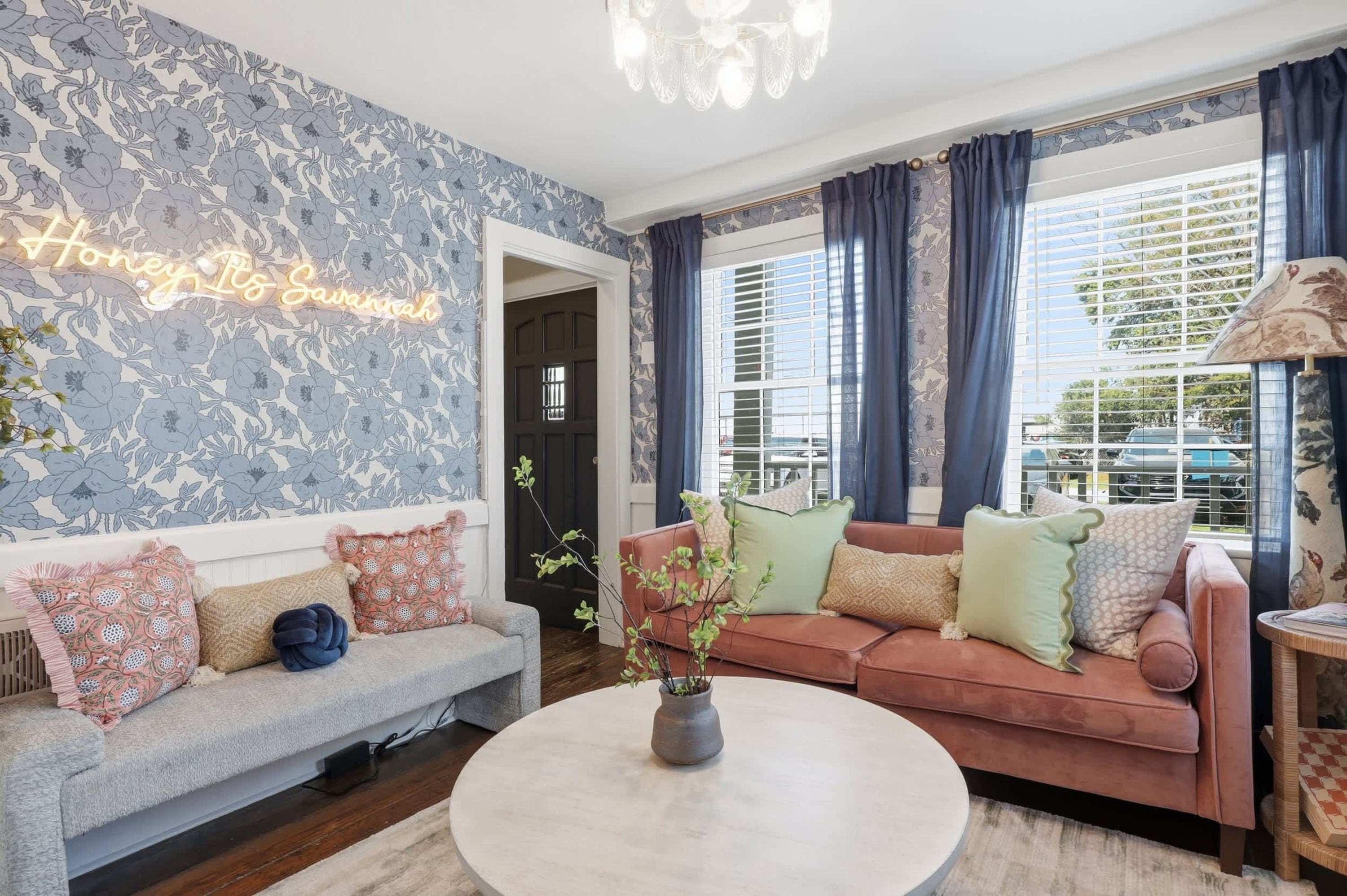 A living room with a floral wallpaper, a sofa, a loveseat, a coffee table, and a chandelier.