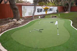 A miniature golf course with a putting green, flags, and a wooden bench. - Giddy Up Getaway Pool Hot Tub Family Fun (San Antonio)