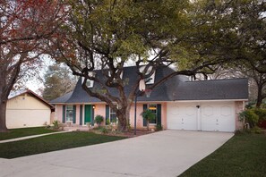 A two-story house with a front garage, a large tree in front, and a well-maintained lawn. - Giddy Up Getaway Pool Hot Tub Family Fun (San Antonio)